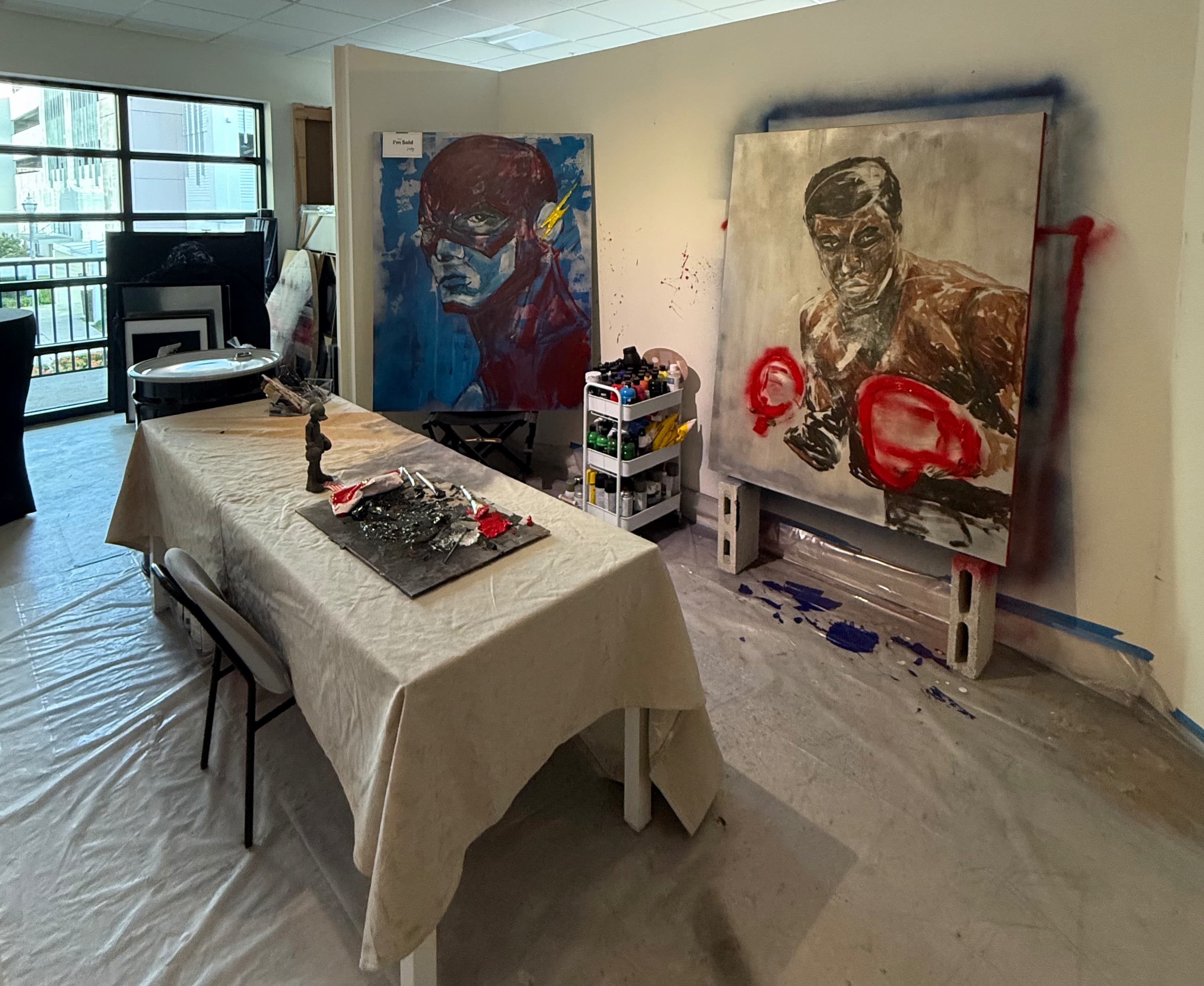 Inside the Lusky studio — paintings in progress, including a boxer with red gloves, beside the work table